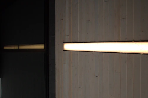 A sleek emergency light fixture installed above a commercial doorway, glowing softly in a dim corridor.