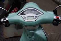A close-up view of the dashboard of a mint green scooter, highlighting the speedometer and handle controls with chrome accents.