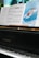 A close-up view of a black K. Kawai piano with sheet music on the music stand. The sheets include musical notes and a cover page for 'The Snowman Easy Piano Suite' featuring an illustration of a snowman and a child flying in the sky. The background displays a blurred green tree seen through a window.