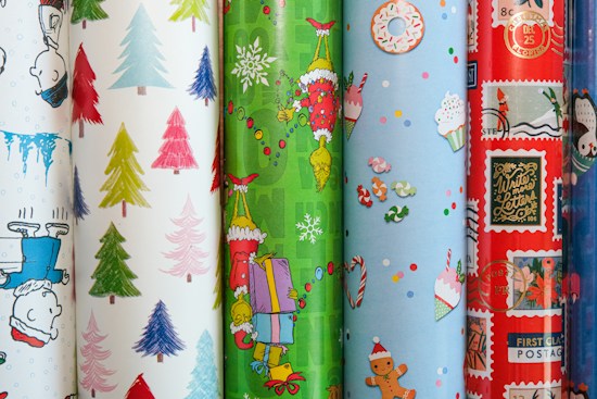 A collection of colorful, festive wrapping papers featuring various holiday-themed designs, such as cartoon characters, Christmas trees, snowflakes, cupcakes, candies, and postal motifs. The designs vary from cute and playful to vintage and classic, with diverse textures and patterns.