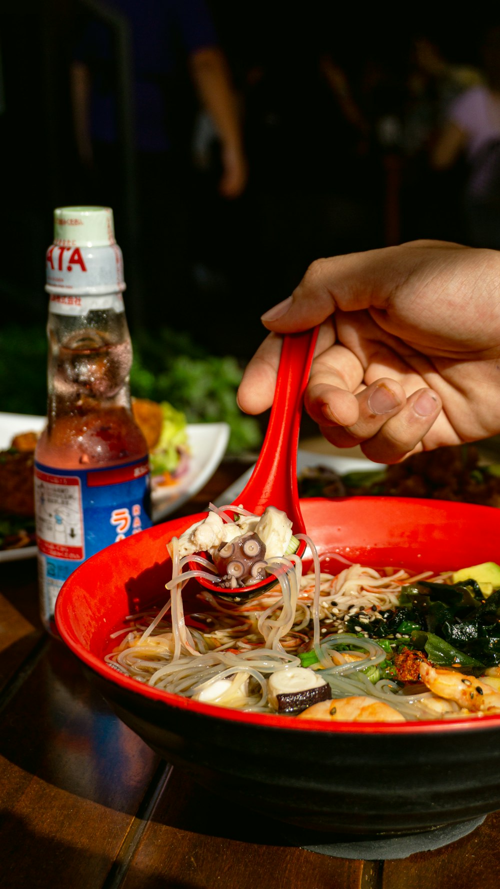 a person holding a red spoon over a bowl of food