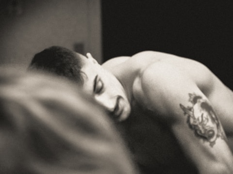 Black and gray tattoo of a wolf howling at the moon on upper arm.