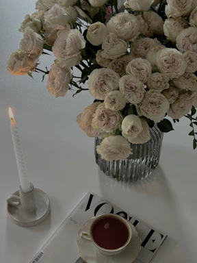 A softly lit vintage teacup candle glowing warmly beside a delicate bouquet of garden roses.