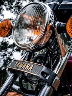 Close-up of a Yamaha motorcycle headlight, with chrome detailing and orange turn signals. The brand name 'Yamaha' is prominently displayed on a black strip across the front.