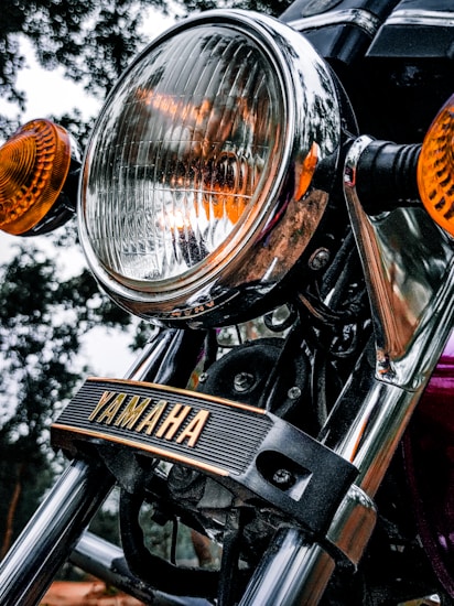 Close-up of a Yamaha motorcycle headlight, with chrome detailing and orange turn signals. The brand name 'Yamaha' is prominently displayed on a black strip across the front.