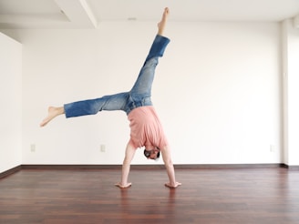 An instructor gently guiding a young performer through a handstand, both smiling in a cozy, welcoming space.