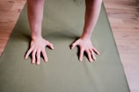 Close-up of Ella’s hands gripping a yoga mat on a hardwood floor.