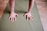 Two hands are placed on a green yoga mat, presumably in a position for a yoga pose or exercise. The floor is wooden with a light brown finish.