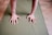 Two hands are placed on a green yoga mat, presumably in a position for a yoga pose or exercise. The floor is wooden with a light brown finish.