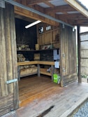 A garden shed door open, revealing neatly stacked supplies and a small workbench inside.