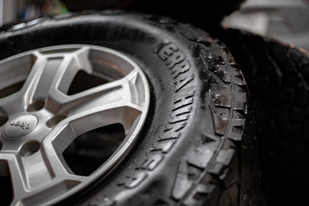 A close-up view of a black tire with visible tread patterns. The tire is labeled 'Terra Hunter' and appears wet, suggesting recent contact with water. Beside the tire is a metallic wheel with a detailed design, exhibiting a silver color.