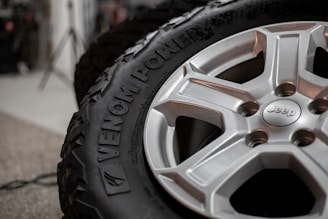 A close-up view of a tire with the brand name 'Venom Power' embossed on the side. The wheel is a silver alloy adorned with a 'Jeep' logo in the center. The background is blurred, highlighting the focus on the tire and wheel.