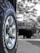 A close-up view of a vehicle tire with the brand name Cooper and model Discoverer AT3 XLT. The tire's treads and grooves are clearly visible, with a shiny metallic hubcap at the center. The background appears to be blurred, featuring a larger vehicle possibly parked or in motion.