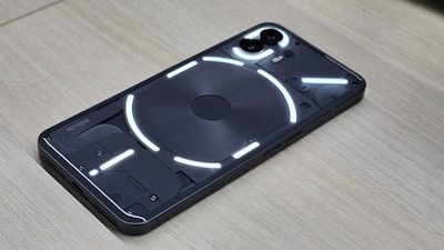 A smartphone displaying a transparent back panel with visible internal components, highlighted by a series of bright white LED strips. The device rests on a wooden surface, and the dual camera module is prominently visible.