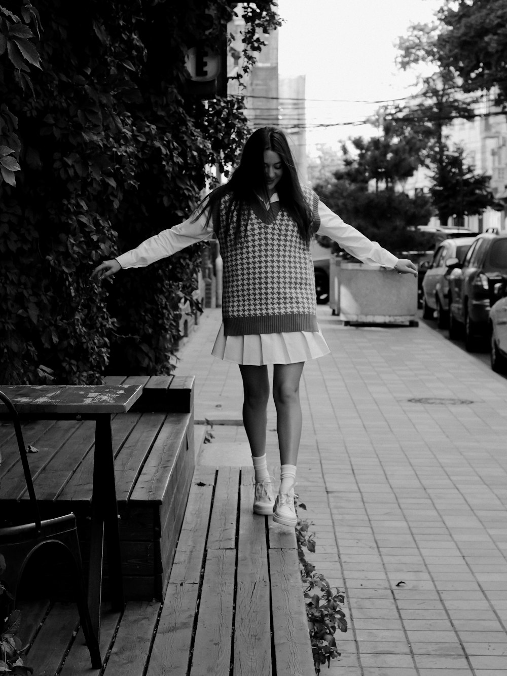 a woman walking down a sidewalk next to a wooden bench