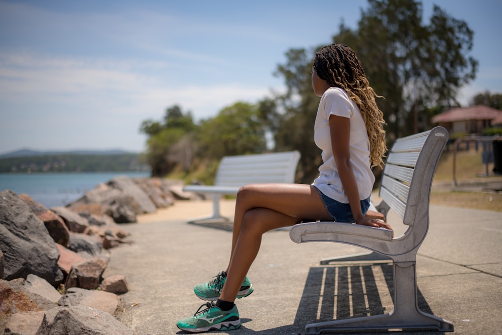 a woman sitting on a bench next to a body of water