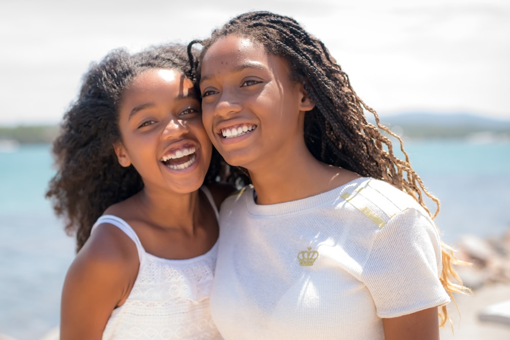 two young women standing next to each other near the ocean