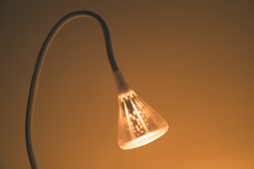 A glowing lamp with a curved neck emits a warm light. The lamp's translucent shade is illuminated from within, creating a cozy ambiance against a minimalistic background.