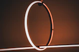 A modern abstract lighting fixture features glowing circular and linear elements, emitting a warm, ambient light. The minimalist design is set against a softly lit, neutral-toned background.