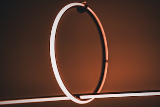 A modern abstract lighting fixture features glowing circular and linear elements, emitting a warm, ambient light. The minimalist design is set against a softly lit, neutral-toned background.