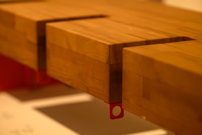 A close-up view of a wooden structure featuring a notched corner design with smooth finishes. The wood grain is visible, and the piece is positioned on a red support, which adds a modern accent to the overall look.