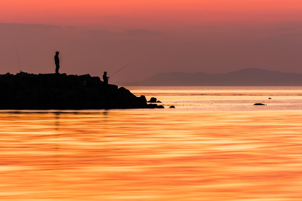 a man fishing at sunset on a rocky outcropping