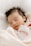 A peaceful sleeping baby wrapped in a soft, light-colored blanket. The baby has dark hair and wears a pink outfit.