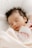 A peaceful sleeping baby wrapped in a soft, light-colored blanket. The baby has dark hair and wears a pink outfit.