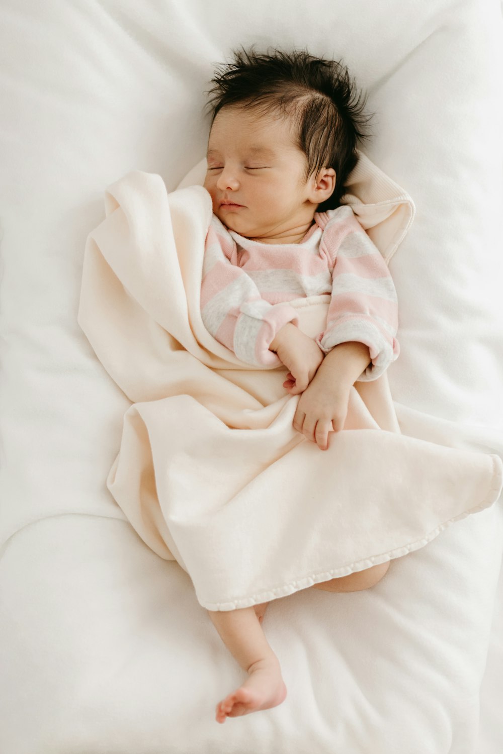 a baby wrapped in a blanket sleeping on a pillow