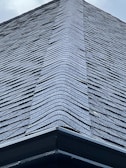 A close-up view of a roof with dark, overlapping shingles creating a textured surface. The shingles appear to be evenly laid with a symmetrical design.