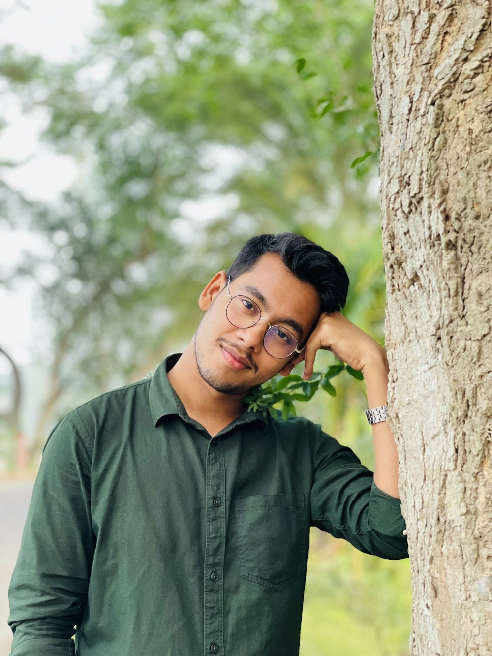 a man wearing glasses leaning against a tree