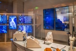 A high-tech laboratory environment featuring multiple digital screens displaying complex graphical data, including a large DNA helix. The room contains advanced laboratory equipment on a sleek table and a chair draped with a white lab coat. Soft lighting and a futuristic aesthetic contribute to the overall ambiance.