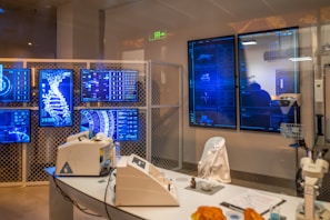 A high-tech laboratory environment featuring multiple digital screens displaying complex graphical data, including a large DNA helix. The room contains advanced laboratory equipment on a sleek table and a chair draped with a white lab coat. Soft lighting and a futuristic aesthetic contribute to the overall ambiance.