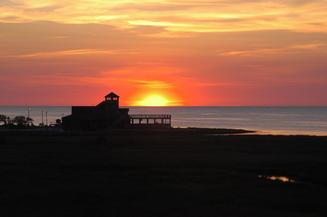 the sun is setting over the ocean with a house in the foreground,