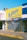 A storefront with a large bright yellow sign that reads 'La Gloria' with additional text indicating it sells clothing for babies, baptisms, and ceremonies. The shop has a closed metal shutter with a striped awning in shades of pink and blue.