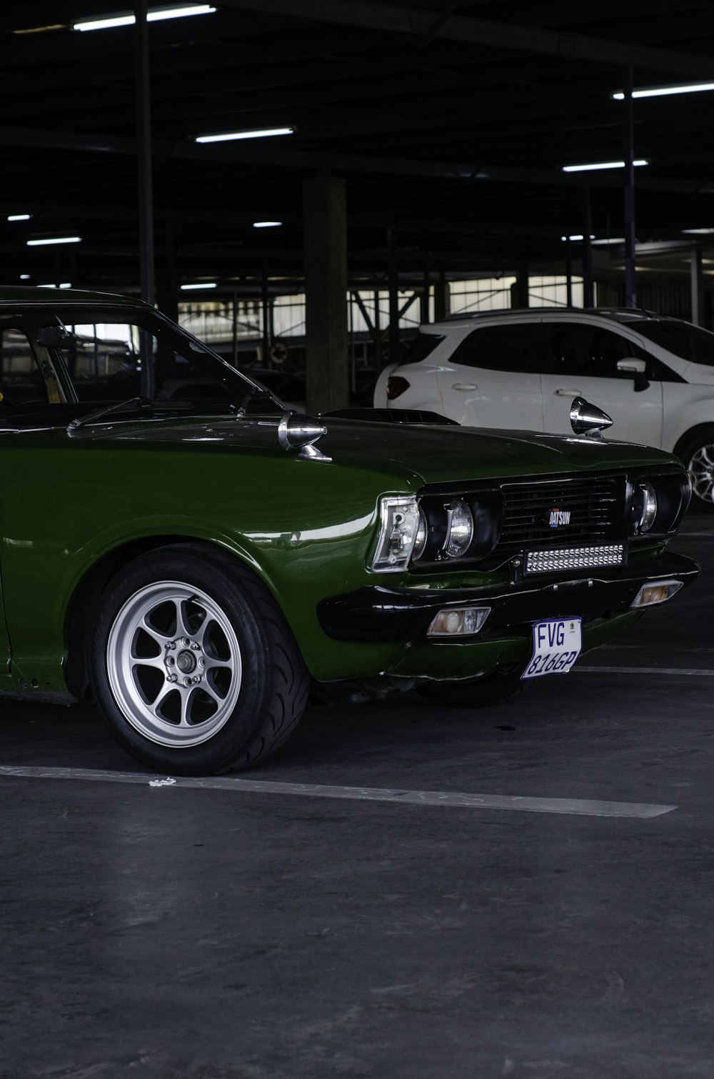 a green car parked in a parking lot next to a white car