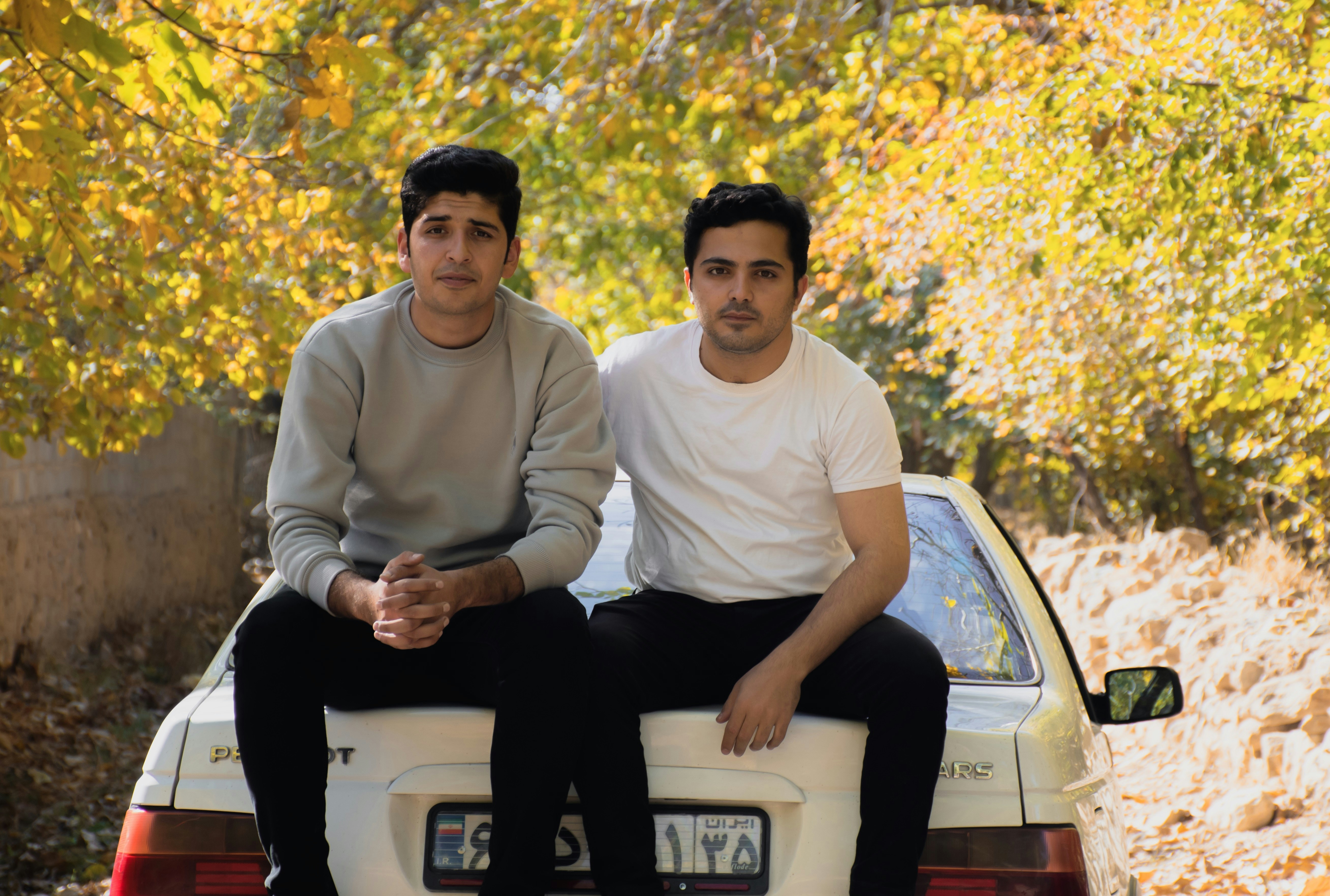 two men sitting on the back of a white car