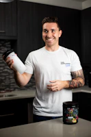 Smiling woman holding a green zupps supplement bottle in a bright kitchen.
