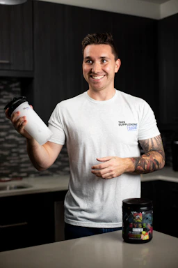 Smiling fitness enthusiast enjoying a post-workout shake with vitaforge branding visible