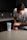 A person in a gray T-shirt is preparing a supplement drink in a modern kitchen. The individual is holding a container labeled 'Legion Pulse' next to a clear shaker bottle with some powder inside. The countertop is clean and smooth, and the background features dark cabinets and a tiled backsplash.