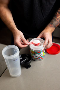 Muscular arm holding a container of muscle gain supplements with red glow effect.