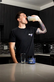 a man drinking a glass of milk in a kitchen