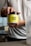 A person holding a container labeled 'Naked Energy' against a blurred interior background. The container has a bright yellow label with black text.