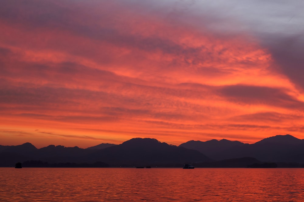 a sunset over a body of water with mountains in the background