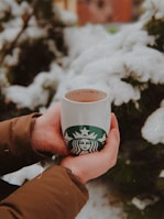 Model outdoors wearing cream-colored gloves, holding a warm cup of coffee.