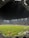 A nighttime soccer match in a large, well-lit stadium. Players in brightly colored jerseys are on the field, surrounded by a large audience in the stands. The scoreboard displays 0-0, indicating the start of the match. The seating area features patterns made by colored seats among the spectators.