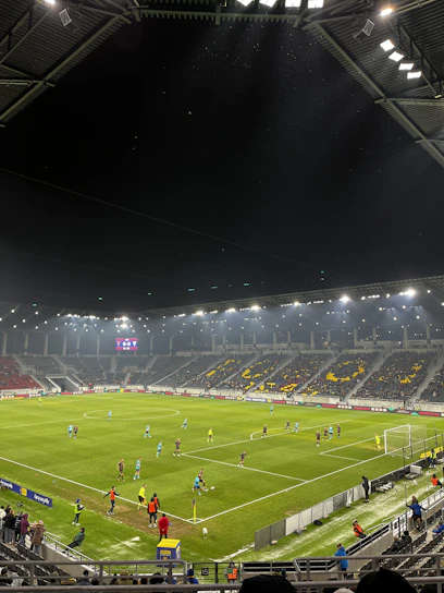 A vibrant scoreboard displaying live soccer match results under stadium lights.