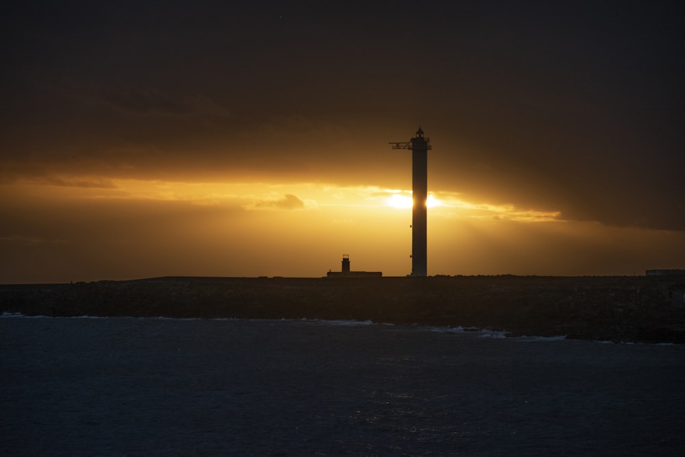 the sun is setting behind a lighthouse on the water