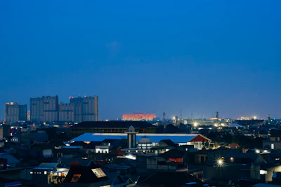 A bustling cityscape viewed from a high rooftop during twilight.