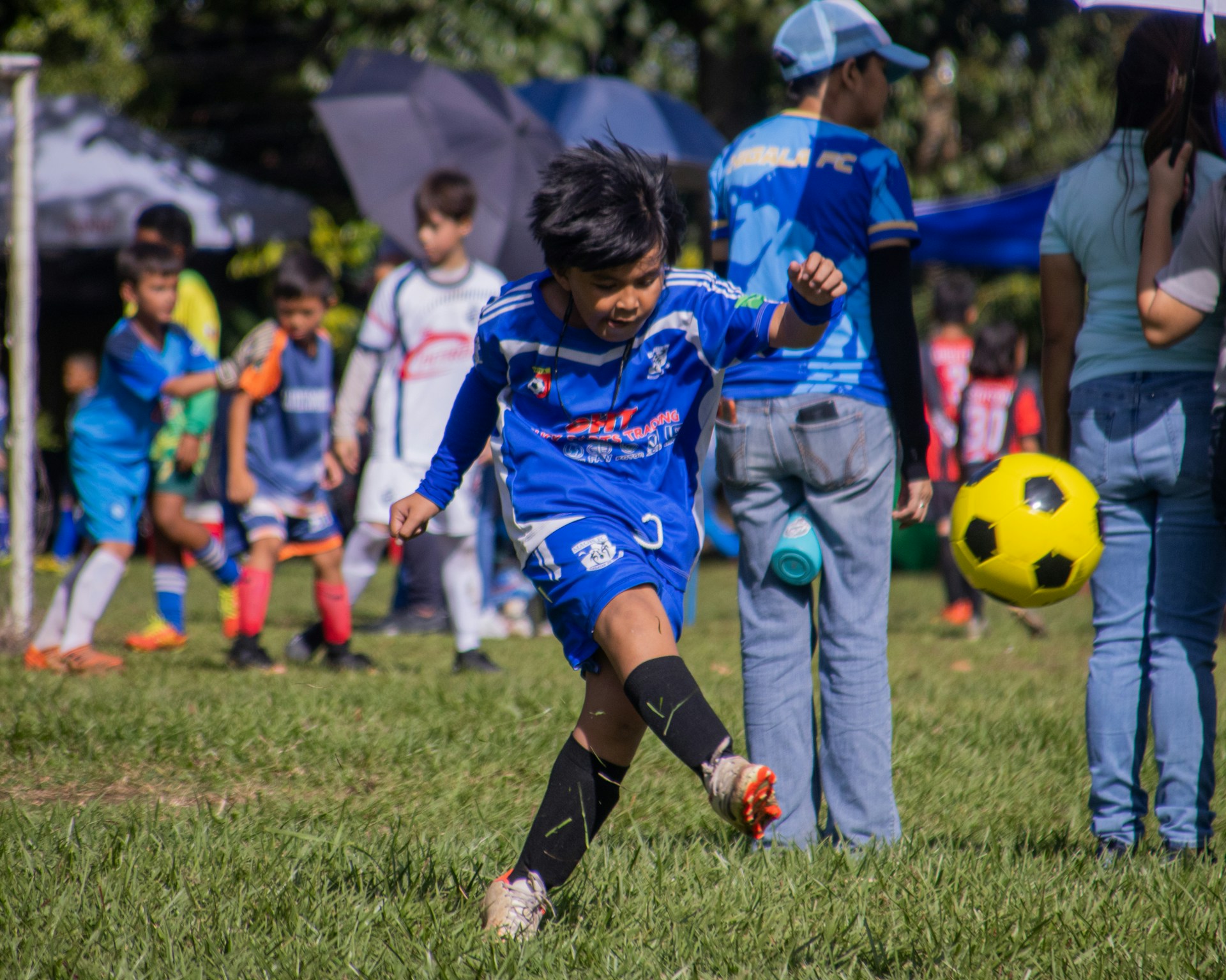 A young boy in a soccer uniform dribbling a ball on a grassy field.